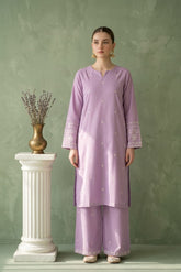 Woman wearing a light purple traditional outfit standing next to a white pedestal with a vase on it against a green wall.