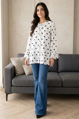 Woman wearing a white blouse with black patterns and blue jeans standing in a living room.