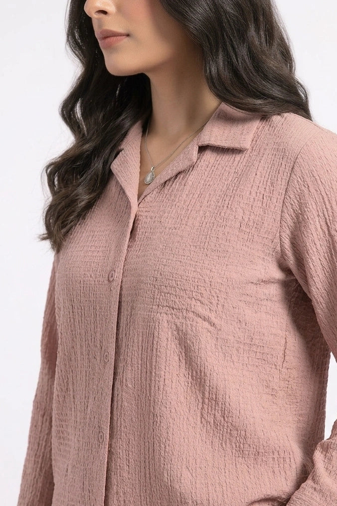 A woman wearing a textured, long-sleeve button-up shirt in a dusty rose pink color, shown from the side against a plain white background.