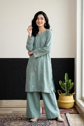 Woman wearing a light blue traditional outfit in a room with a black and white wall and a cactus plant.