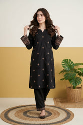 Woman wearing a black traditional outfit with intricate patterns against a yellow wall.