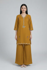 Woman wearing a mustard yellow outfit with intricate designs on a plain background