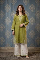 Woman wearing a green embroidered kurta with white pants against a patterned blue background