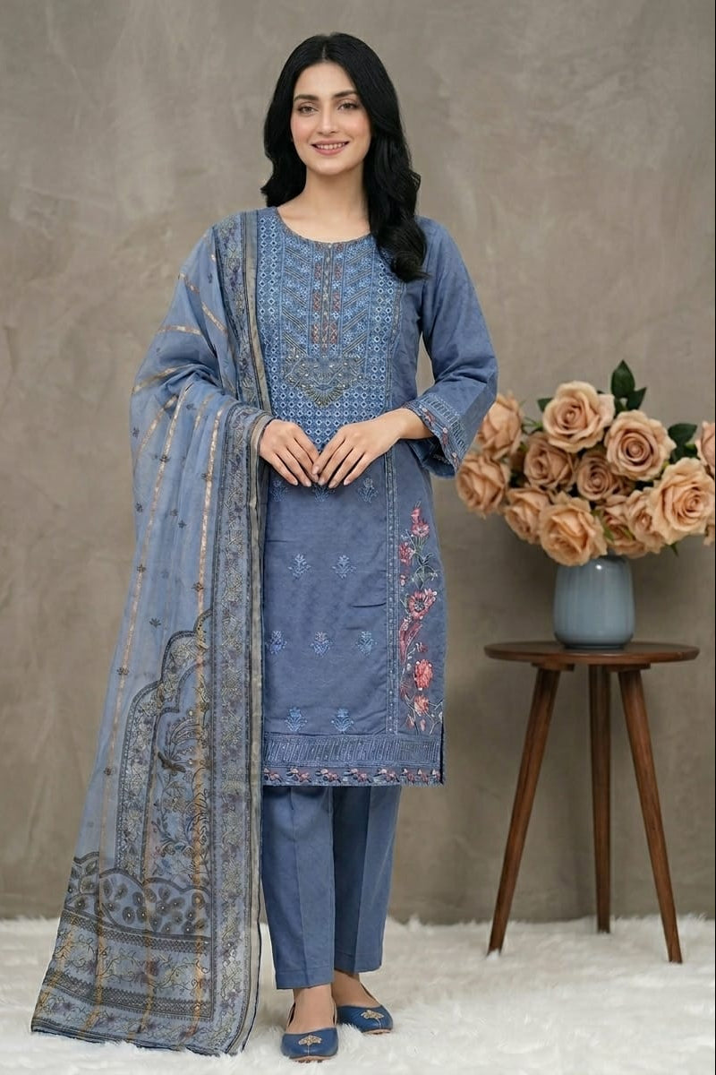 Woman wearing a blue embroidered outfit with a matching dupatta, standing next to a vase of flowers on a wooden table.