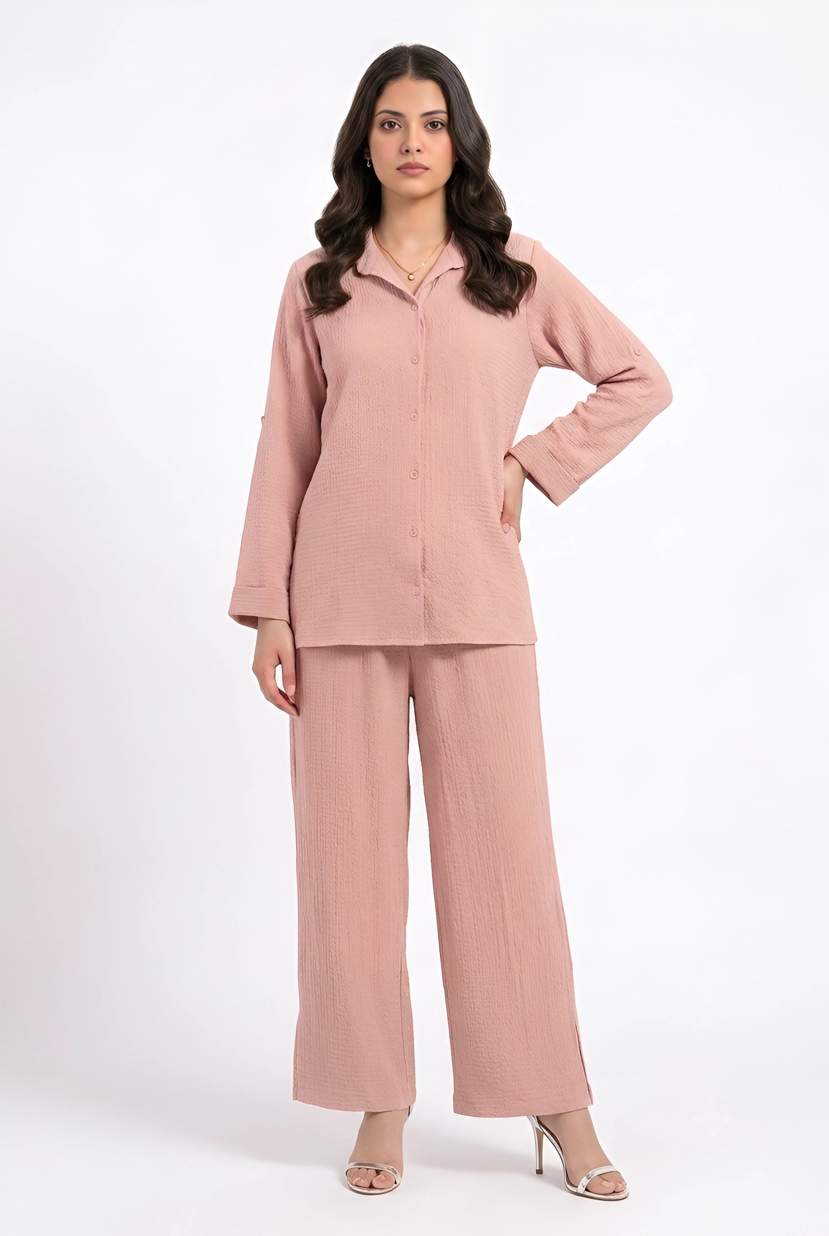 A woman modeling a dusty pink two-piece lounge set consisting of a long-sleeve button-front top and matching wide-leg pants, photographed against a plain white studio background.
