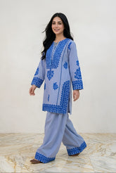 Woman wearing a blue and gray traditional outfit with intricate patterns on a white background