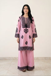 Woman wearing a pink embroidered outfit with black patterns on a white background