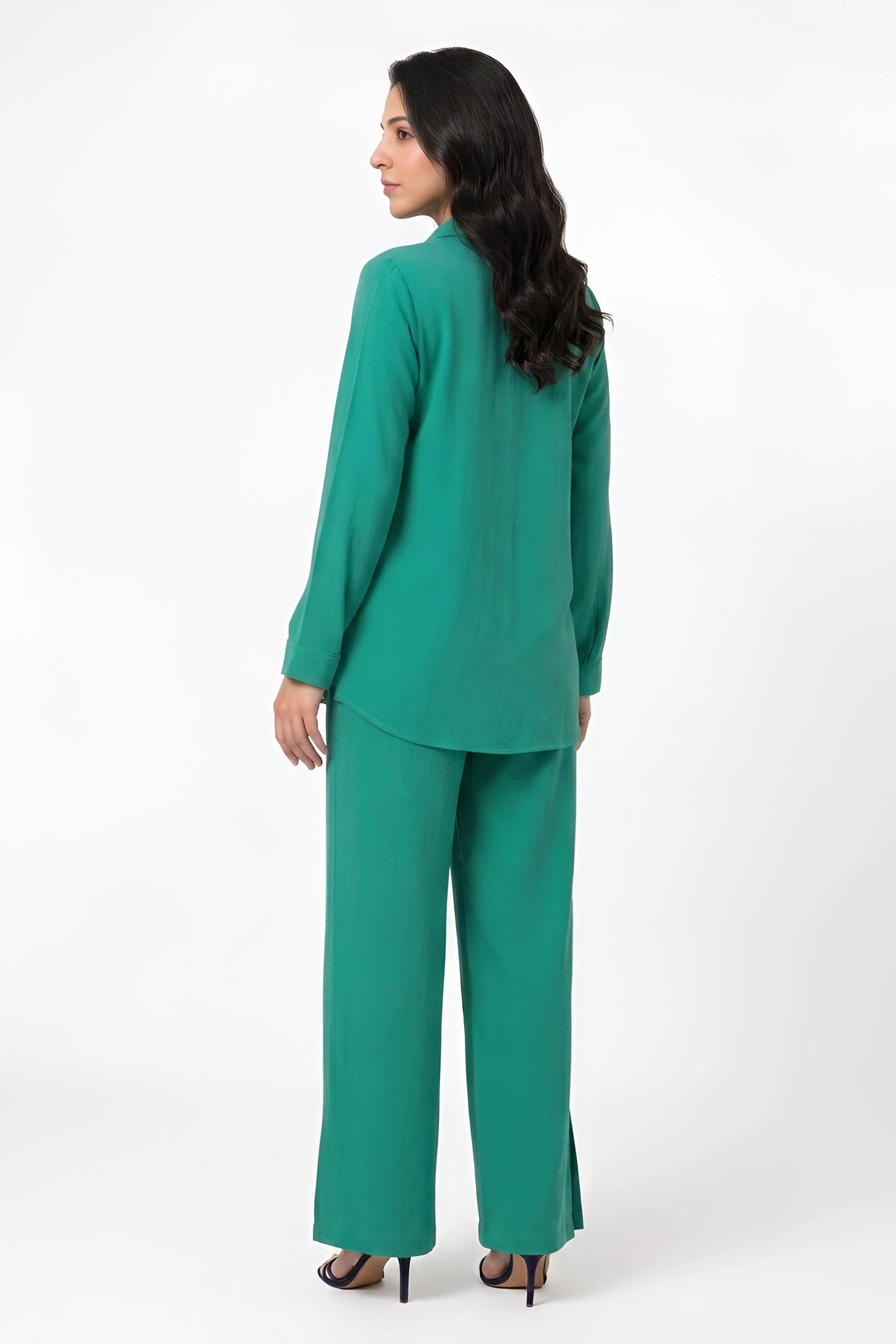 A woman wearing a matching green two-piece set consisting of a long-sleeve top and wide-leg pants, shown from a rear three-quarter view against a plain white studio background.