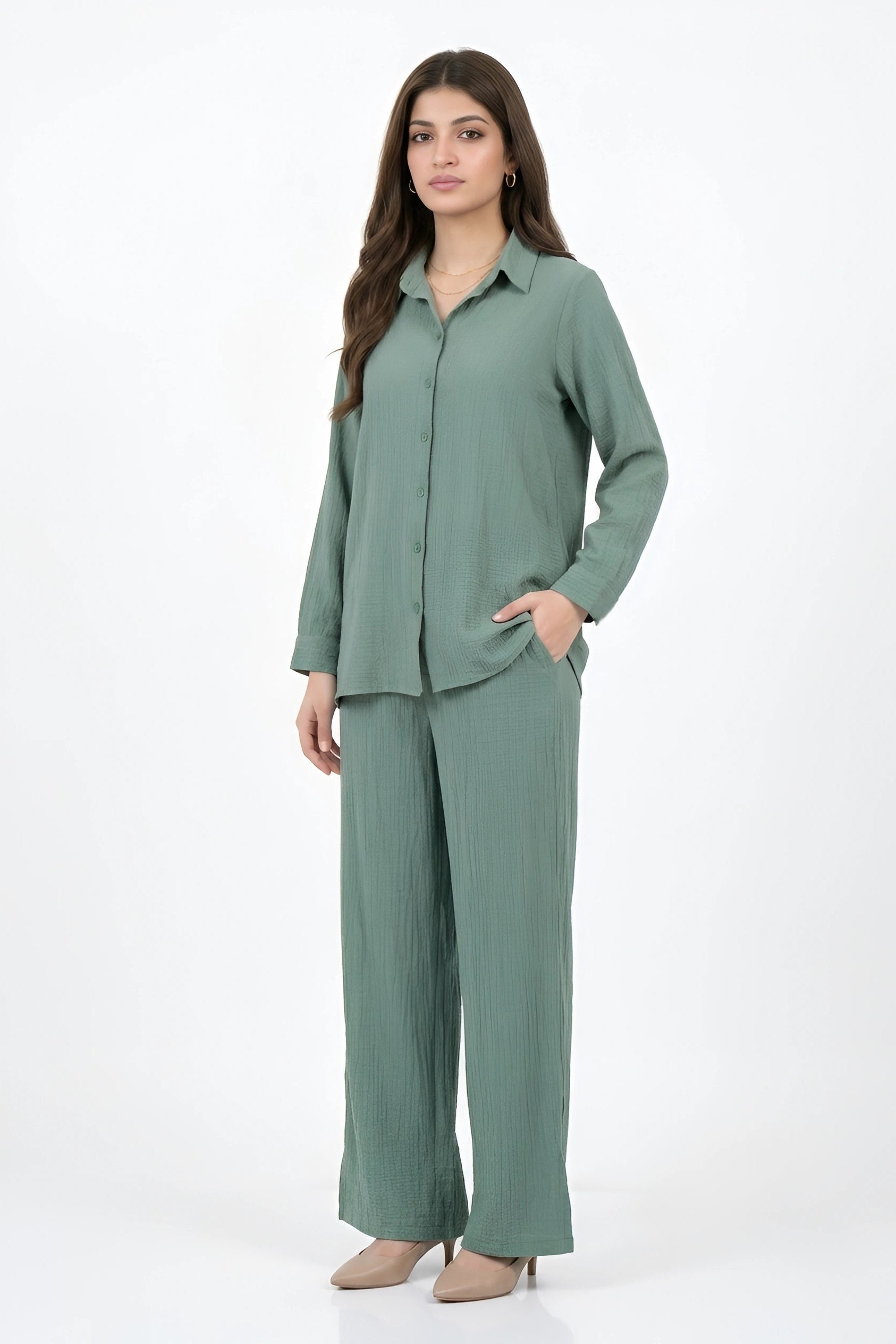 A woman modeling a matching sage green two-piece set consisting of a long-sleeve button-up shirt and wide-leg trousers, photographed against a plain white studio background.