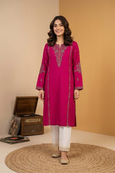 Woman wearing a pink embroidered kurta with white pants standing in a room with a brown suitcase and records.