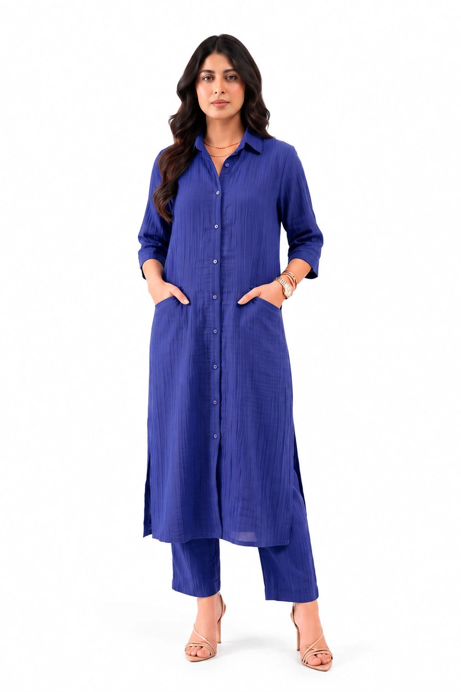 A woman modeling a long-sleeved, button-front kurta in a rich royal blue color, paired with matching blue cropped pants and beige high-heeled sandals, set against a plain white background.