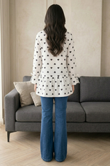 Person wearing a white shirt with black heart patterns and blue jeans standing in a living room.