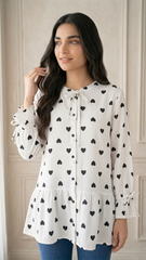 Woman wearing a white blouse with black heart patterns against a neutral background