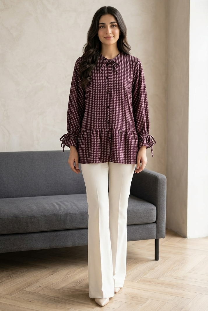 Woman wearing a checkered blouse and white pants standing in a room with a gray sofa and large window.