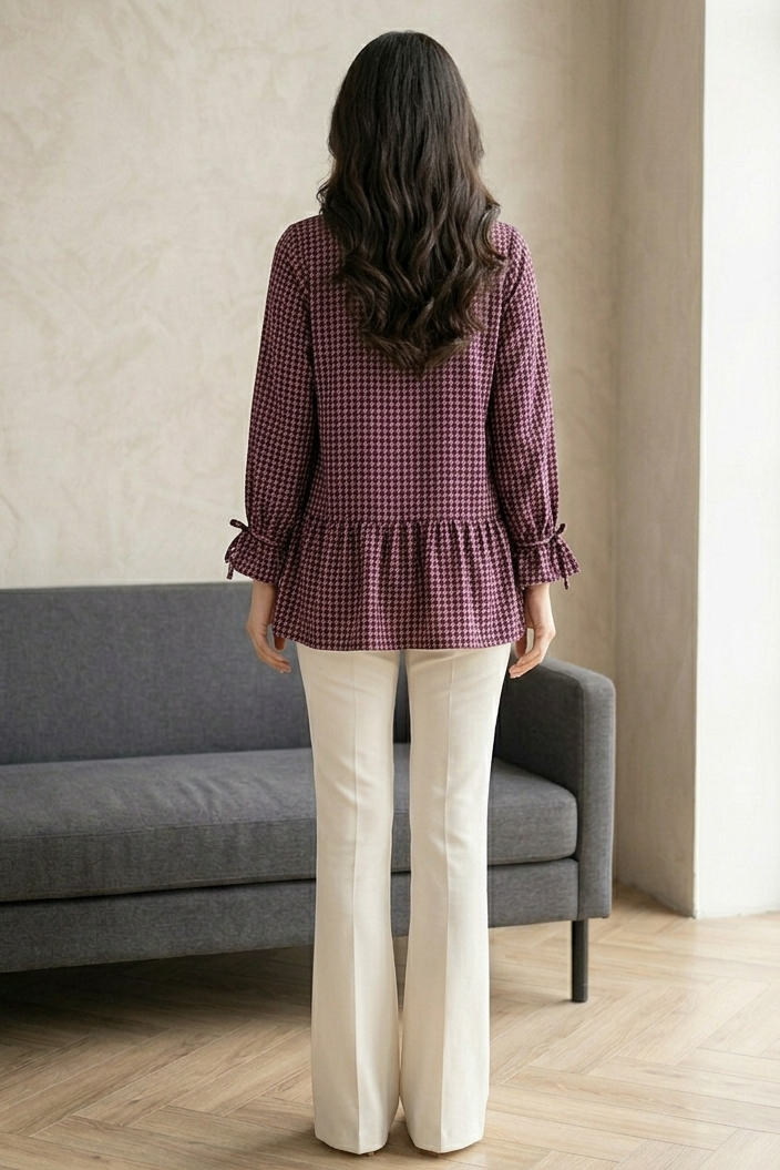 Woman wearing a checkered blouse and white pants standing in a room with a gray sofa and large window.
