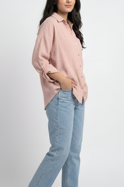 A woman modeling a light pink button-up shirt with light blue jeans, standing against a plain light gray studio background.