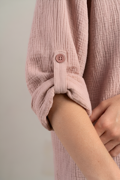 Close-up of a dusty pink textured cotton gauze shirt with rolled-up sleeves, featuring a matching button detail and a soft neutral background.