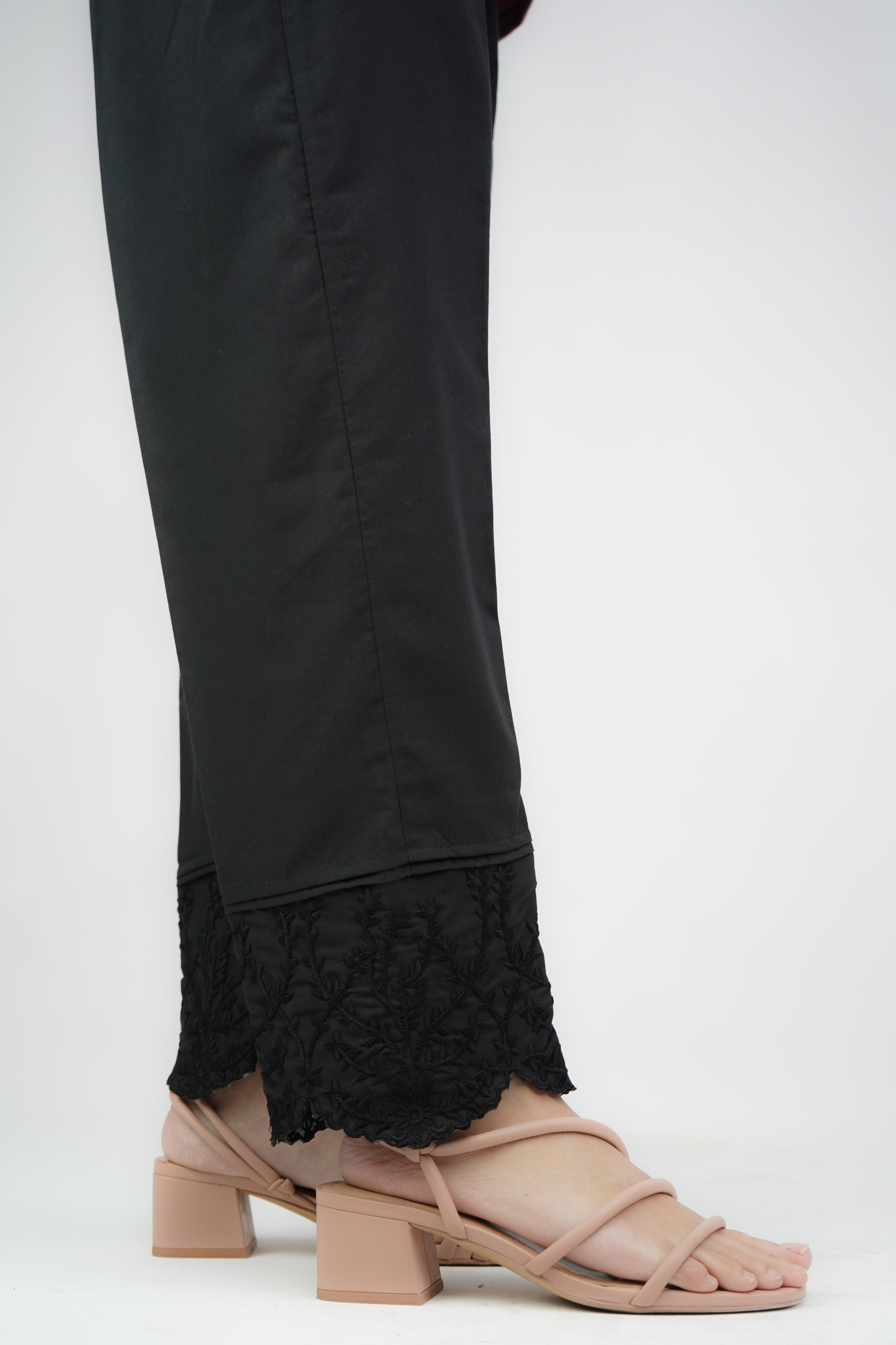 A close-up of black cigarette pants with embroidered details and lace at the cuffs, featuring a mid-rise waist.