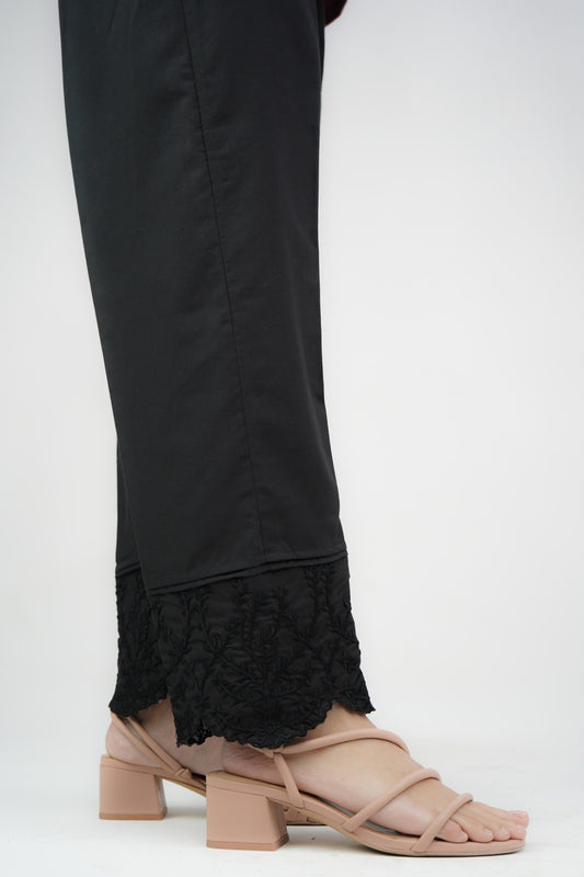 A close-up of black cigarette pants with embroidered details and lace at the cuffs, featuring a mid-rise waist.