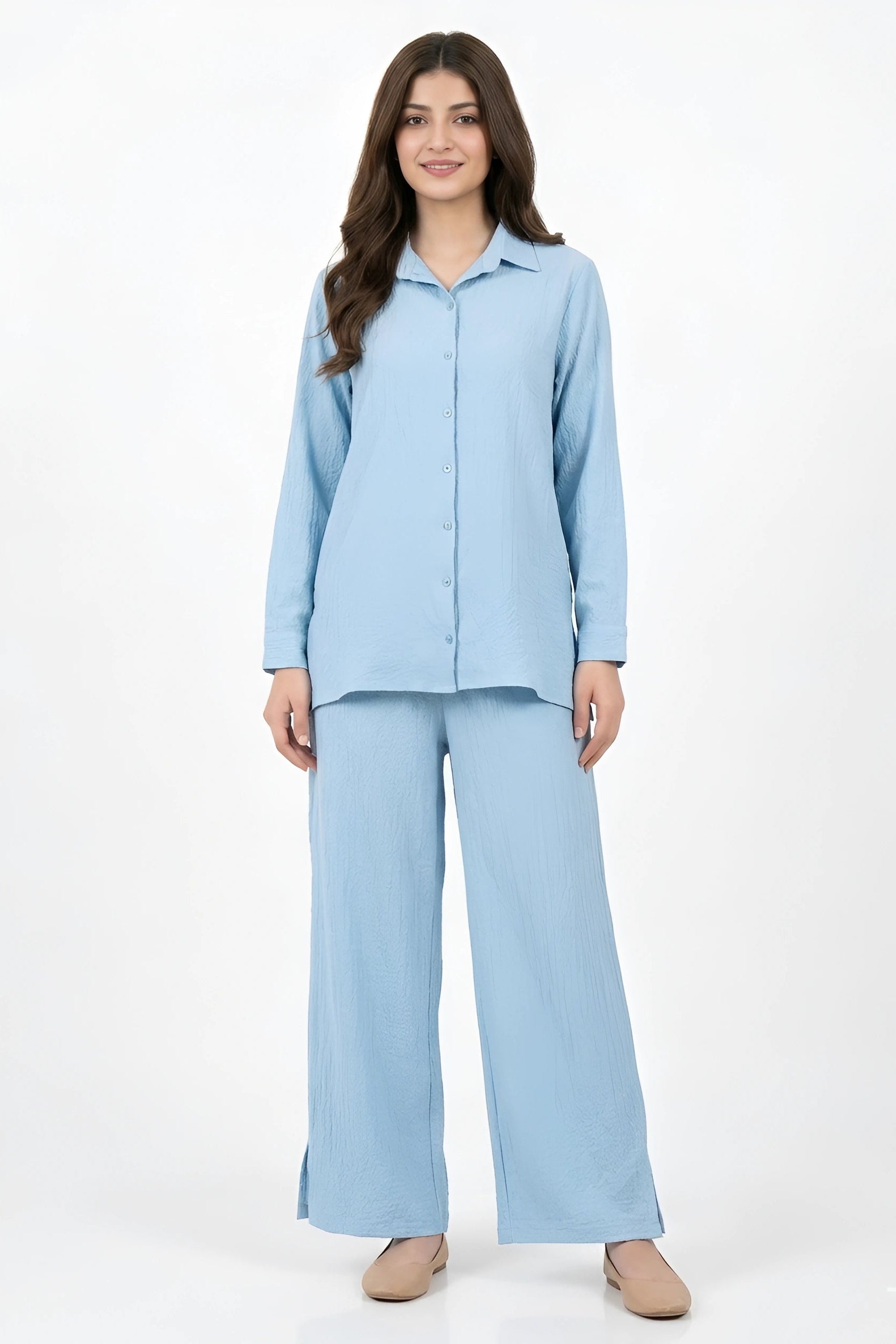 A woman modeling a light blue two-piece pajama set consisting of a long-sleeve button-up shirt and matching wide-leg pants, photographed against a plain white studio background.