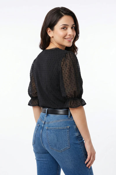 Woman wearing a black blouse with sheer sleeves and blue jeans on a white background