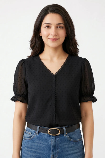 Woman wearing a black blouse with sheer sleeves and blue jeans on a white background