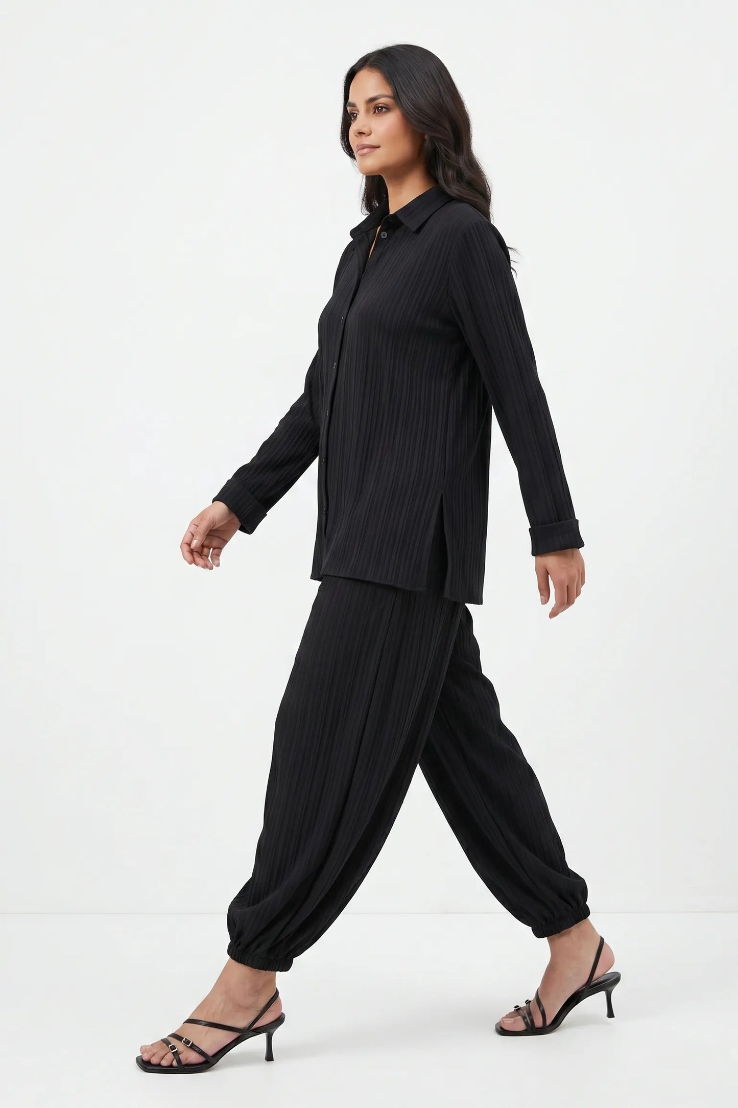 Woman wearing a black outfit with a jacket and harem pants on a white background