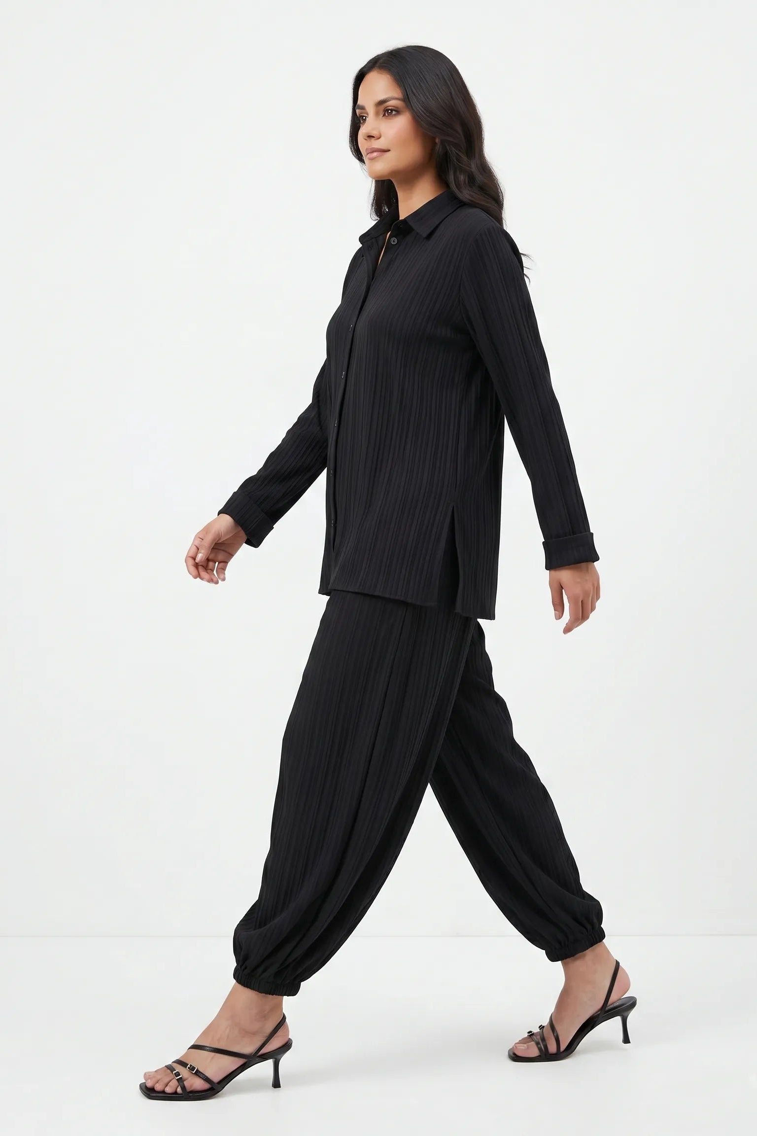 Woman wearing a black outfit with a jacket and harem pants on a white background