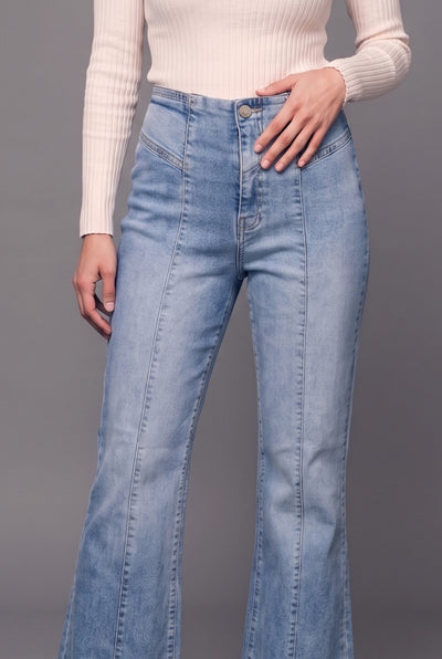 A model wearing light blue high-waisted flare jeans with a cream ribbed knit top, shown from the chest down against a solid gray studio background.