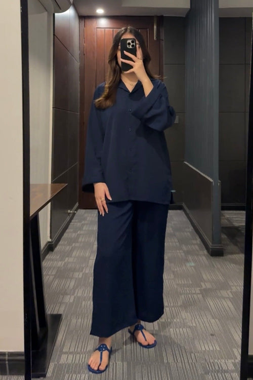 Person taking a mirror selfie wearing a navy outfit in a room with a wooden door and gray walls.