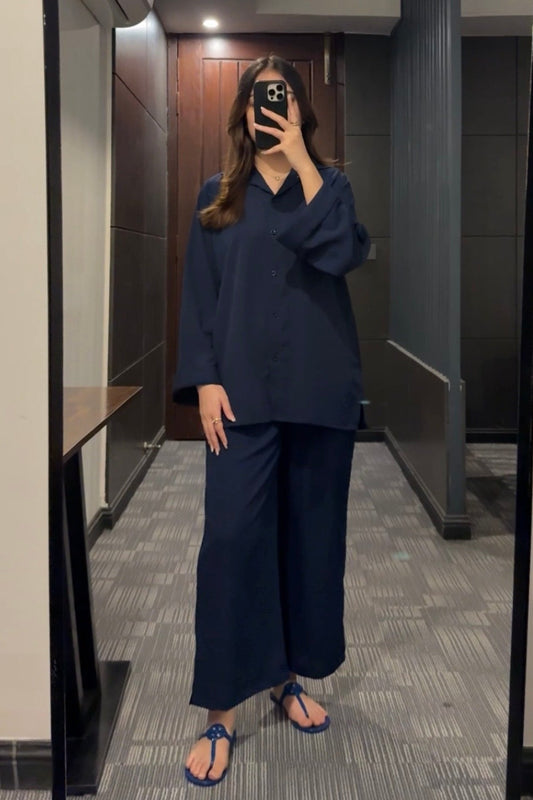 Person taking a mirror selfie wearing a navy outfit in a room with a wooden door and gray walls.