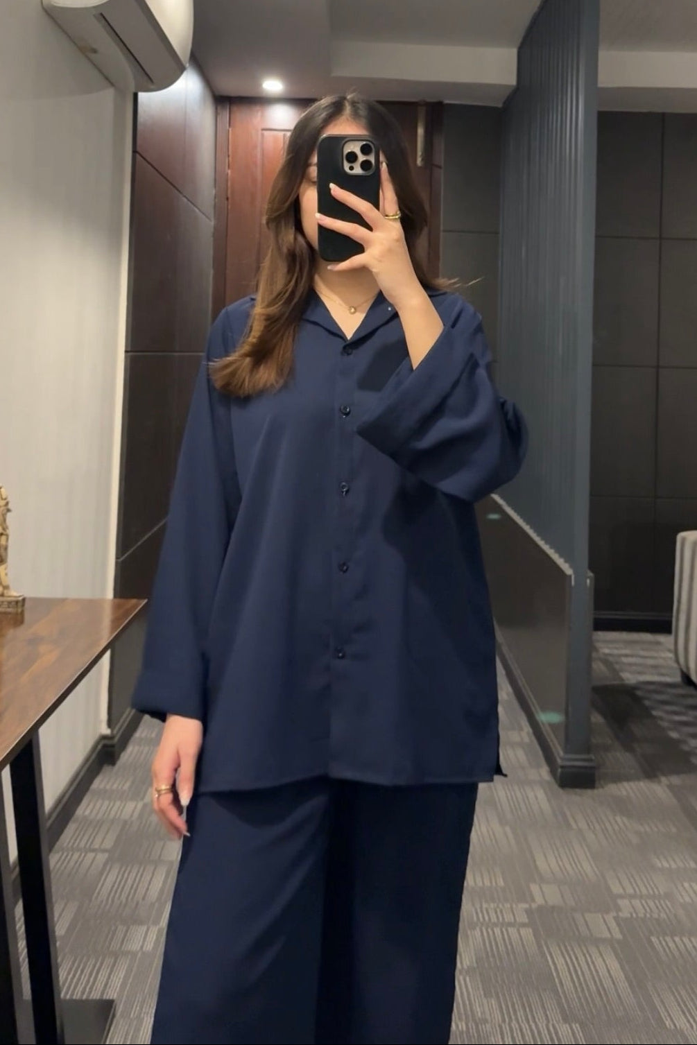 Person wearing a navy blue outfit taking a mirror selfie in an indoor setting.