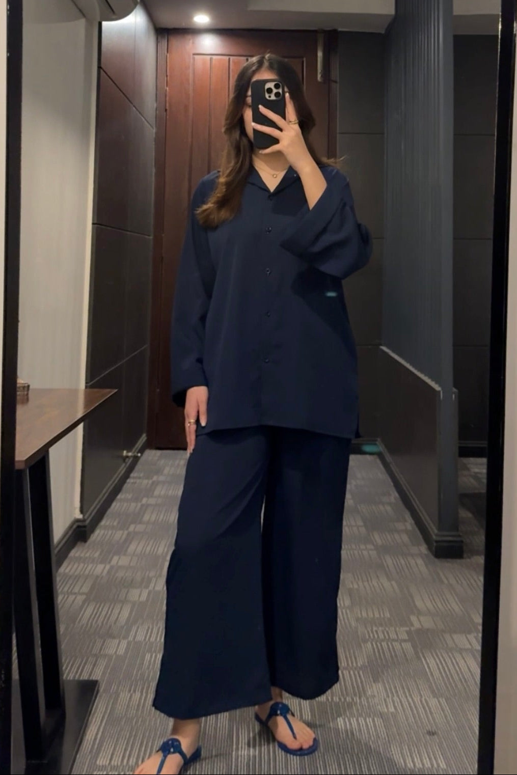 Person wearing a navy outfit taking a mirror selfie in a room.