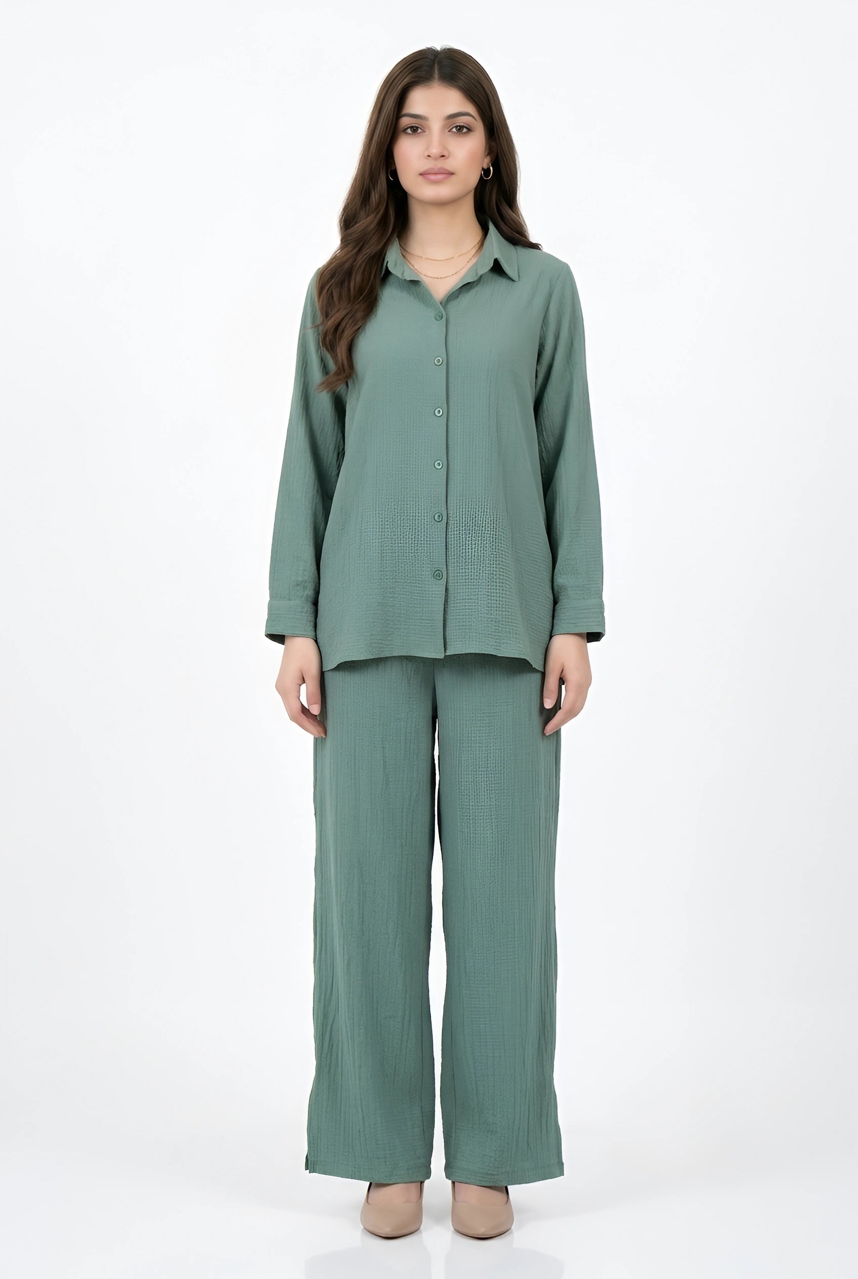 A woman modeling a matching sage green two-piece set consisting of a long-sleeve button-up shirt and wide-leg trousers, photographed against a plain white studio background.