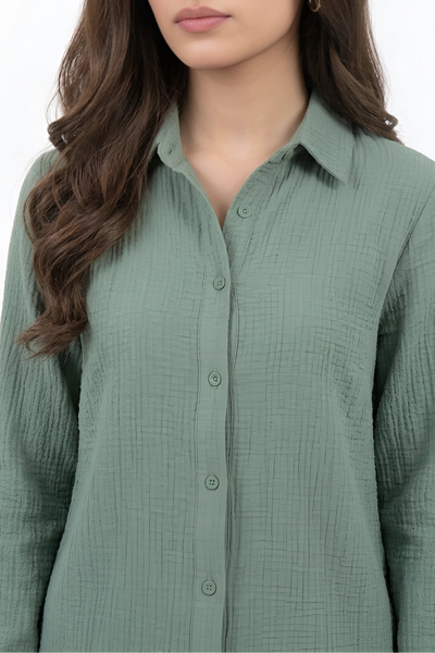 A woman wearing a sage green long-sleeve button-up shirt with a textured crinkle fabric, shown against a plain white background.