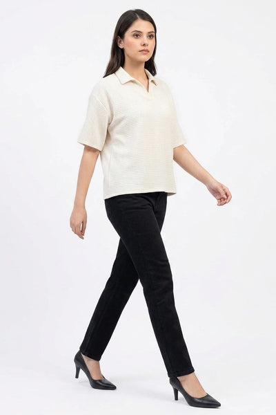 Full-length side view of a model walking in an off-white waffle knit top and black jeans.