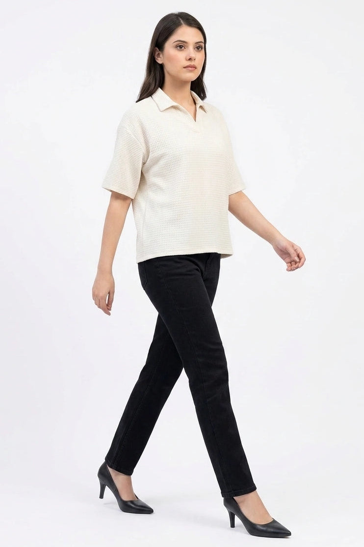 Full-length side view of a model walking in an off-white waffle knit top and black jeans.
