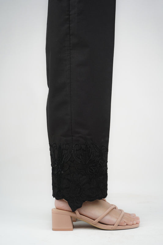 A pair of black embroidered cigarette pants on a model who is facing away from the camera.