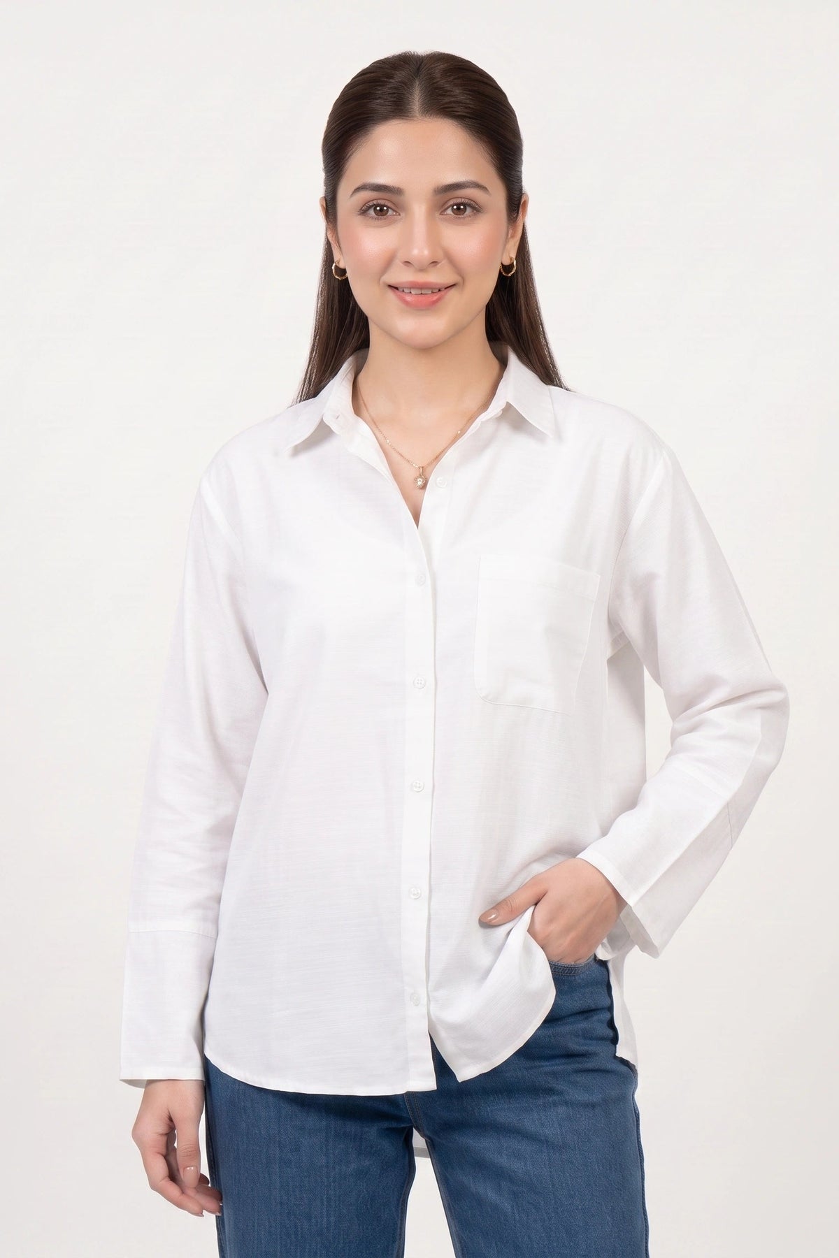 A woman modeling a white long-sleeve button-up shirt with a chest pocket, paired with blue jeans, against a plain white studio background.