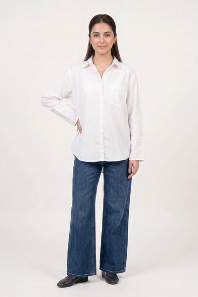 A woman modeling a white long-sleeve button-up shirt with dark blue wide-leg jeans and black shoes, standing against a plain off-white studio background.
