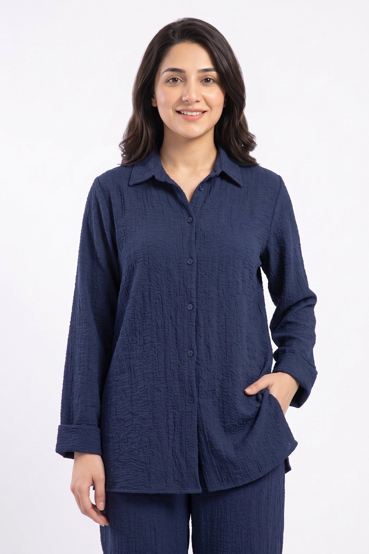 A woman modeling a dark navy blue textured long-sleeve button-up shirt with matching navy pants against a plain white studio background.