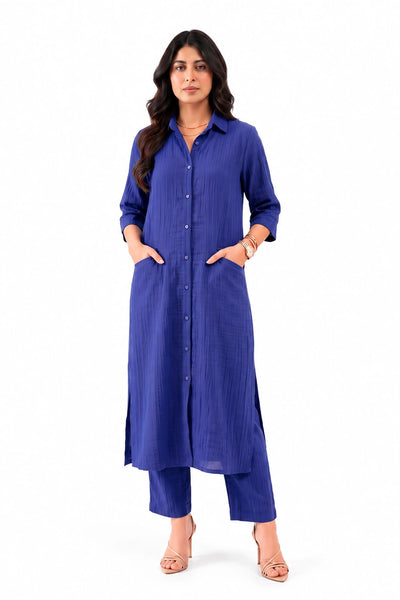 A woman modeling a long-sleeved, button-front kurta in a rich royal blue color, paired with matching blue cropped pants and beige high-heeled sandals, set against a plain white background.