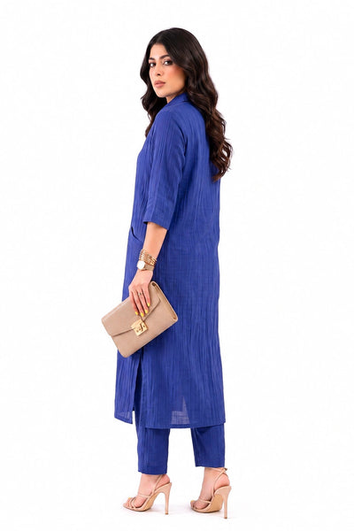 A woman modeling a royal blue two-piece kurta set with matching pants, holding a beige clutch bag, against a plain white background.