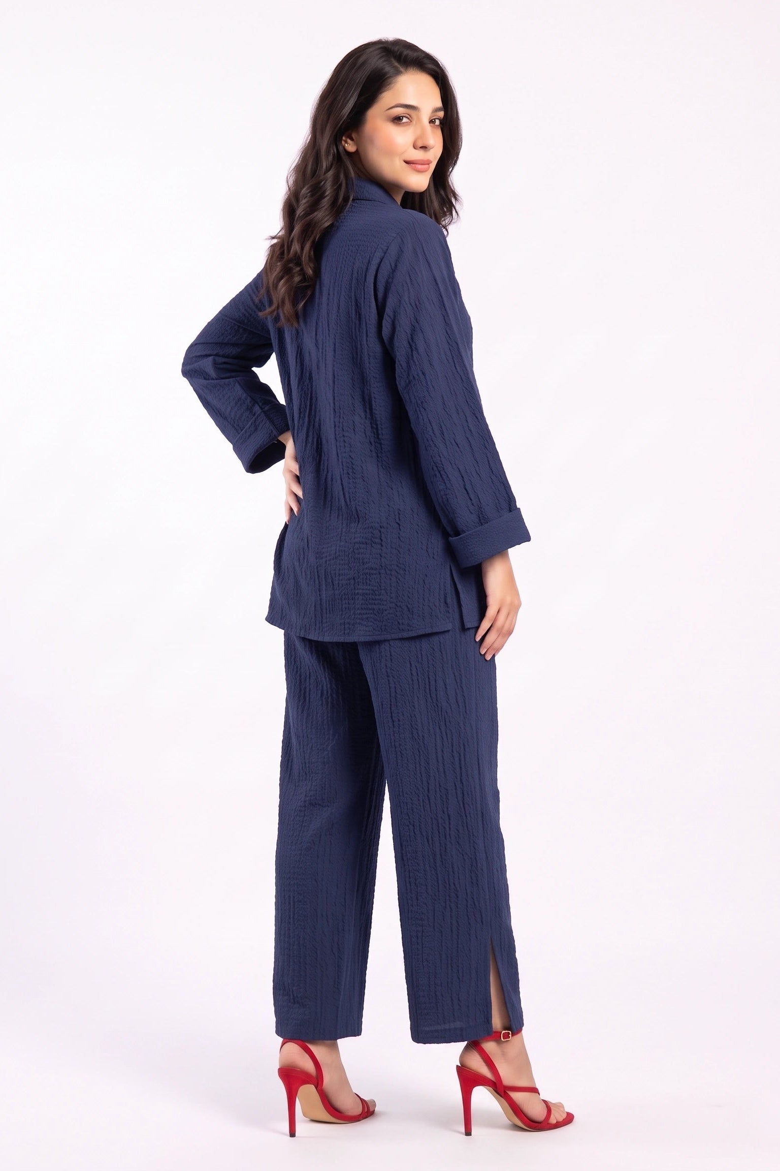 A woman modeling a navy blue two-piece set consisting of a textured long-sleeve top and matching wide-leg trousers, paired with red high-heeled sandals, against a plain white studio background.