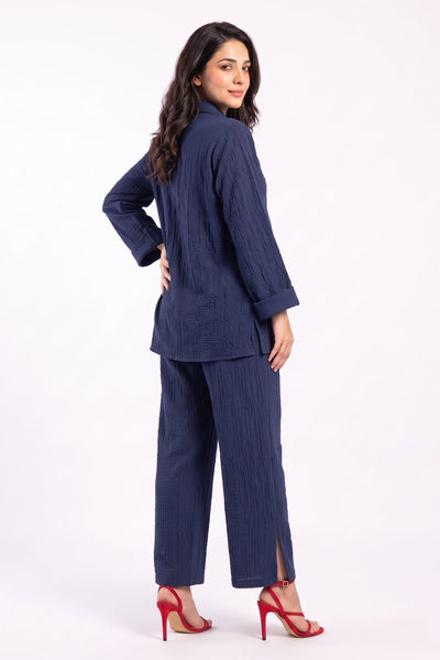 A woman modeling a navy blue two-piece set consisting of a textured long-sleeve top and matching wide-leg trousers, paired with red high-heeled sandals, against a plain white studio background.