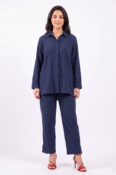 A woman modeling a matching navy blue two-piece set consisting of a long-sleeve button-up shirt and wide-leg cropped pants, styled with red high-heeled sandals against a plain white studio background.