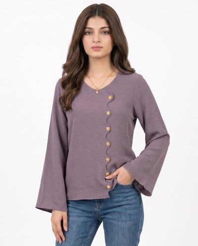 A woman modeling a dusty purple long-sleeve top with a decorative row of gold buttons down the front, paired with blue jeans, against a plain white background.