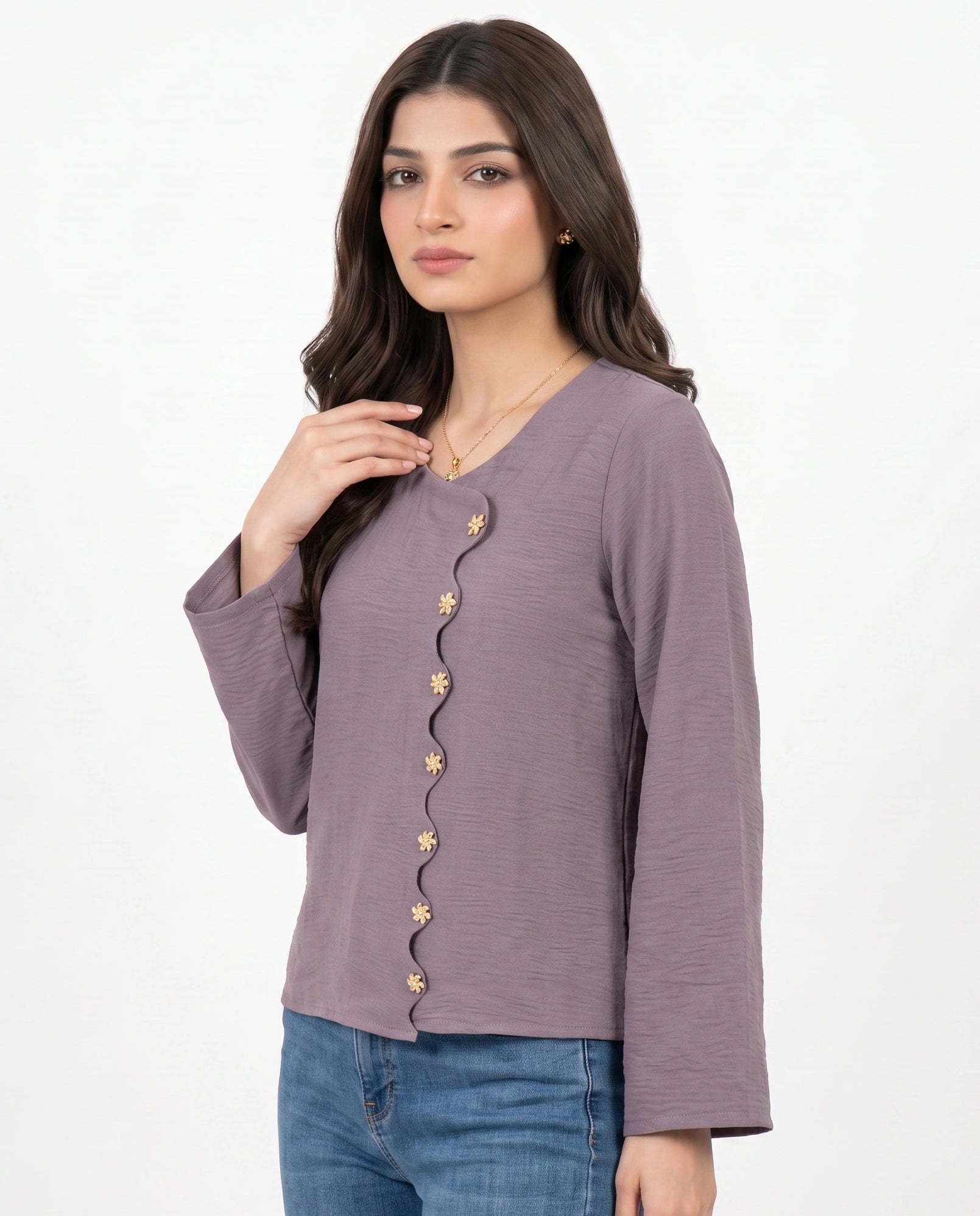 A woman modeling a mauve-colored long-sleeve top with gold decorative buttons down the front, paired with blue jeans, against a plain white background.