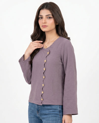 A woman modeling a mauve-colored long-sleeve top with gold decorative buttons down the front, paired with blue jeans, against a plain white background.