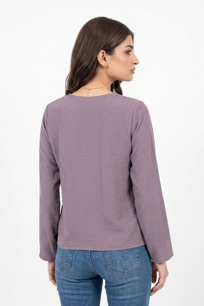 A woman shown from the back wearing a long-sleeve, crew-neck top in a dusty mauve-purple color, paired with blue jeans, against a plain white studio background.